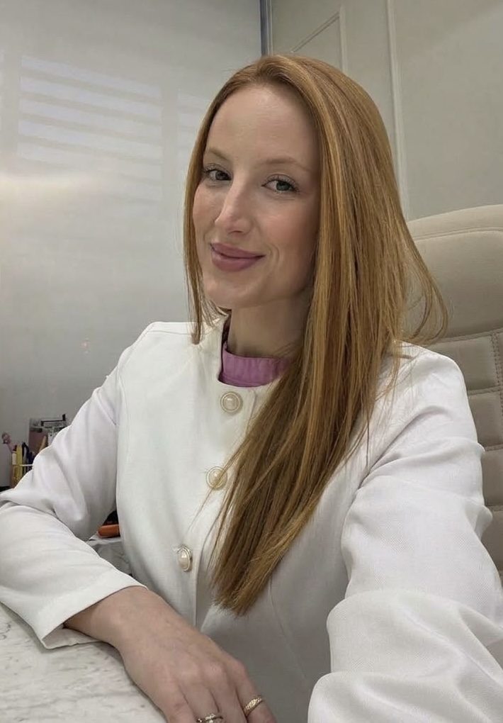 Dra. Ana Gabardo sorrindo no consultório, de jaleco branco